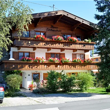 A charming building in Alpine style with blooming balcony boxes. Surrounded by green countryside and a clear blue sky.