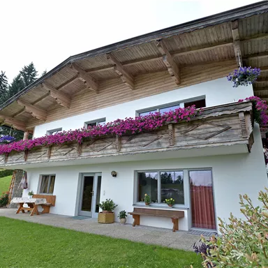 A pretty house with a balcony adorned with colorful flowers. The garden is green and invites you to relax.