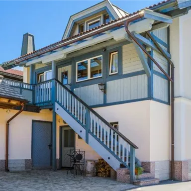 A charming house with a staircase and blue shutters. The clear sky and surrounding architecture give the building an inviting character.
