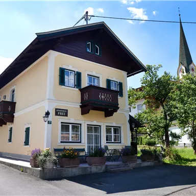 A charming house with a balcony and green windows. In the background, you can see a church tower and trees.