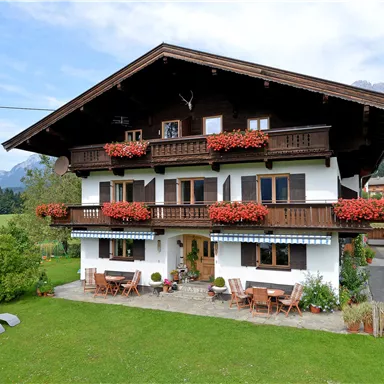 A beautiful alpine house with a large garden. It has balconies with red flowers and a picturesque landscape in the background.