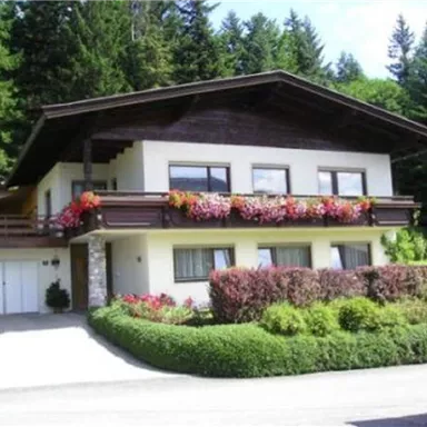 A beautiful house with a wooden roof and colorful flower balconies. Surrounded by green bushes and forest.