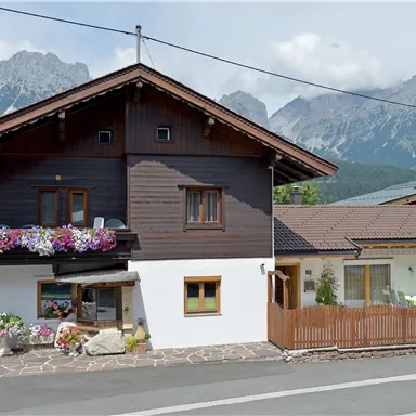 A traditional house with flowers in the windows. Impressive mountains can be seen in the background.