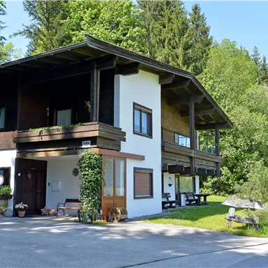 A charming house in a rural setting, surrounded by trees and grass. The clear sky and the sun create a pleasant atmosphere.