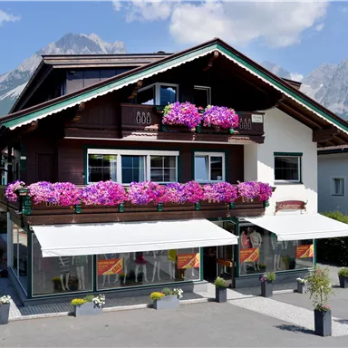A charming wooden building with colorful flower boxes and balconies. Impressive mountains can be seen in the background.