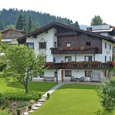 A charming house in alpine style, surrounded by green meadows and trees. The terrace is adorned with blooming flowers.
