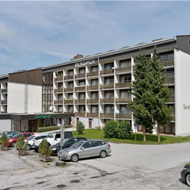 Ein modernes Hotelgebäude mit mehreren Stockwerken und Balconen. Vor dem Hotel parken mehrere Autos in einer begrünten Umgebung.