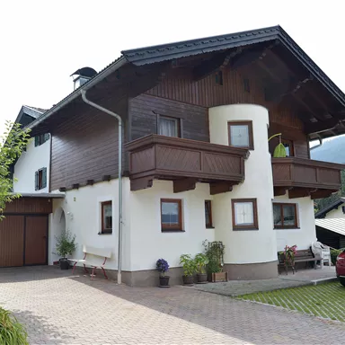 A beautifully designed two-story house with a balcony. The surroundings are well-maintained with lawn and flowers.