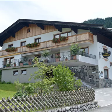 A beautiful country house with wooden elements and many plants. It is located in a quiet environment with green meadows and trees.