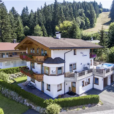 Ein charmantes Haus im Alpenstil, umgeben von grünen Wäldern und Hügeln. Es hat einen Balkon und einen Pool im Garten.
