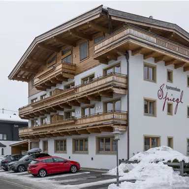 A charming hotel with wooden balustrades and several balconies. It is located in a snow-covered landscape.