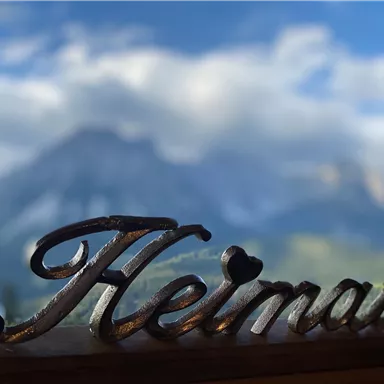 A beautiful landscape with mountains in the background. In the foreground stands the word "Home" in curved script.