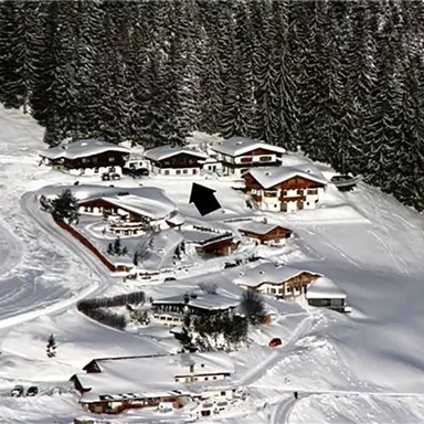 Eine malerische Winterlandschaft mit schneebedeckten Bergen und traditionellen Chalets. Die Umgebung ist ruhig und von -Nadelbäumen umgeben.