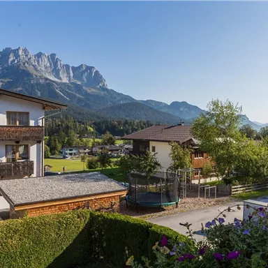 Beautiful mountain landscape with clear blue sky and green meadows. In the foreground, one can see typical alpine buildings and a well-maintained garden.