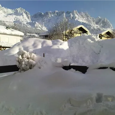 A snowy landscape with high mountains in the background. The snow covers the roofs and the ground.