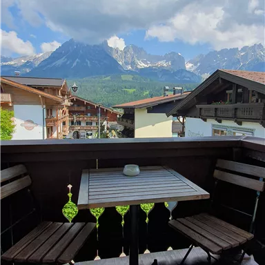A cozy balcony with a table and two chairs. In the background, impressive mountains and a picturesque landscape can be seen.