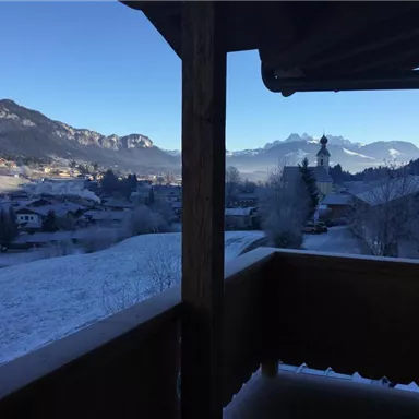 A winter landscape with snow-covered hills and mountains in the background. Through a window, the view of a small village and a church can be seen.