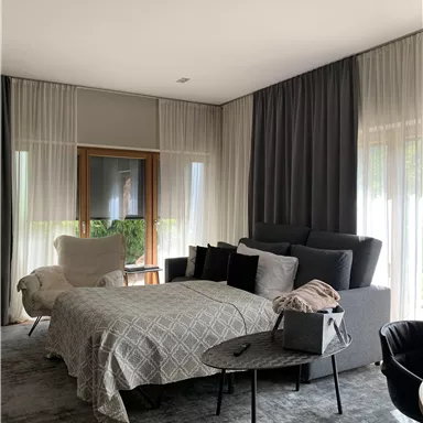 Ein modernes Schlafzimmer mit einem gemütlichen Bett und stilvollen Möbeln. Große Fenster lassen viel Tageslicht herein und schaffen eine helle Atmosphäre.