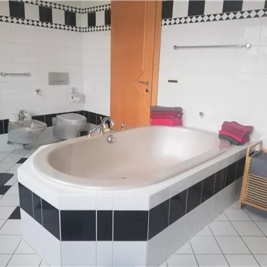 Ein modernes Badezimmer mit einer großen Badewanne und eleganten Fliesen in Schwarz und Weiß. Handtücher in verschiedenen Farben liegen auf einem Stuhl.