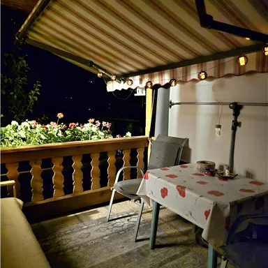 An inviting balcony with a table and chairs. Flowers create a cozy atmosphere at night.