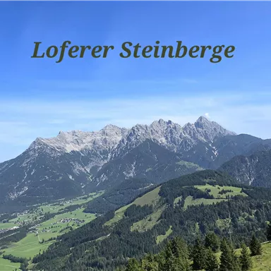 A breathtaking view of the Loferer Steinberge with green meadows in the foreground. The sky is blue and cloudless.