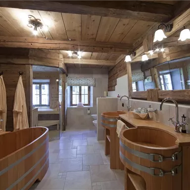 A modern bathroom with wooden details and two round wooden baths. The walls are brightly tiled, and large windows provide plenty of natural light.