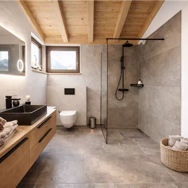 Ein modernes Badezimmer mit Holzdecke und eleganten Fliesen. Es enthält eine begehbare Dusche, ein Waschbecken und eine gemütliche Atmosphäre.