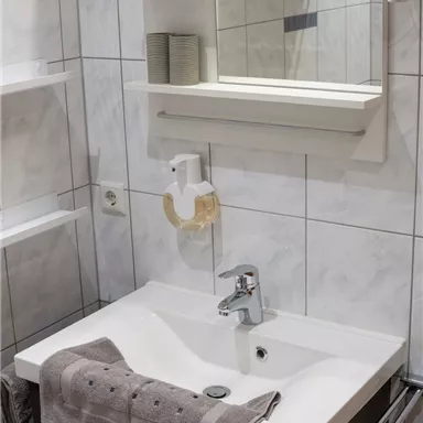 A modern bathroom with a white sink and a mirror. Towels are neatly placed on the sink and the shelves.