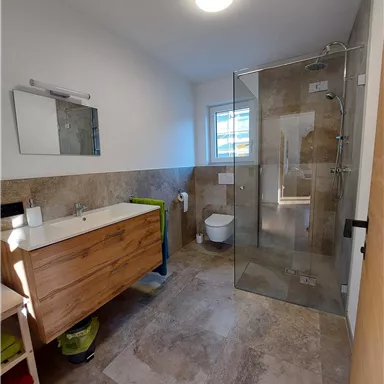 A modern bathroom with a glass shower and a wooden sink. White walls and well-lit, with a stylish, clean design.