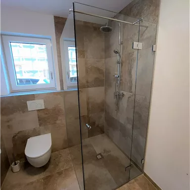 A modern bathroom with a glass shower and a toilet. The walls are decorated with neutral, light tiles.