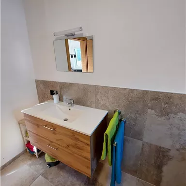 A modern bathroom with a wooden sink and a large mirror. Towels in various colors hang on the wall.