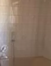 Ein Badezimmer mit einer Badewanne und einer Dusche. Die Wände sind gefliest, und es gibt Holzregale für Aufbewahrung.