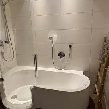 A modern bathroom with a freestanding bathtub and shower. The walls are brightly tiled, and a wooden shelf complements the design.