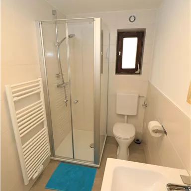 A modern bathroom with a shower, a sink, and a toilet. The walls are bright, and a towel rack is present.