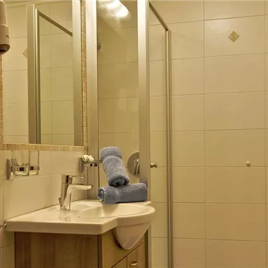 A bright bathroom with a shower, sink, and mirror. On the washstand, there are two blue towels.