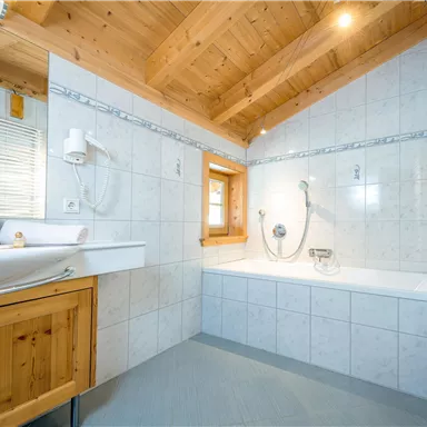 A modern bathroom with wood elements and bright tiles. The bathtub and shower are prominently displayed, and plenty of light comes in through the windows.