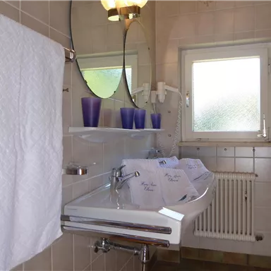 Ein modernes Badezimmer mit einem Waschbecken, Handtüchern und einer großen Spiegel. Es gibt Fenster, die natürliches Licht hereinlassen.