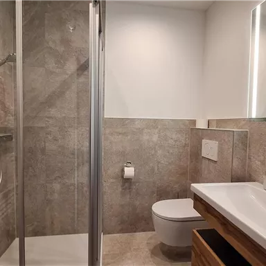Ein modernes Badezimmer mit einer Glasdusche und einem eleganten Waschbecken. Die Wände sind in neutralen Erdtönen gehalten und es gibt genügend Licht durch große Fenster.