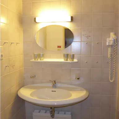 Ein einfaches Badezimmer mit einem runden Spiegel über einem Waschbecken. Die Wände sind gefliest und das Licht ist an der Wand montiert.
