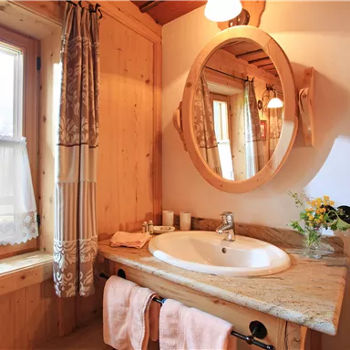 A cozy bathroom with wood paneling and a large mirror. The windows provide a view outside, and there are fresh flowers on the sink.