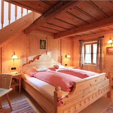 A cozy bedroom with wooden walls and a large bed. The warm lights create an inviting atmosphere.