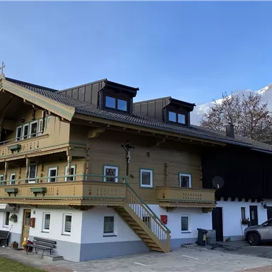 Ein traditionelles Bauernhaus aus der Region mit typischem Balkon. Im Hintergrund sieht man das Bergmassiv des Wilden Kaisers.