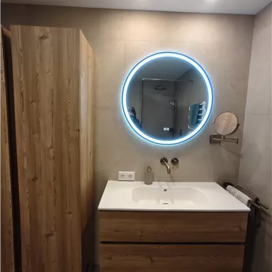 A modern bathroom with wooden cabinets and an elegant sink. An illuminated round mirror complements the stylish design.