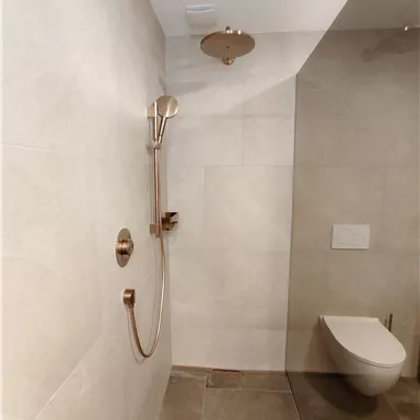 A modern bathroom with an elegant shower and golden fittings. The walls are tiled in light tones, creating a calming atmosphere.