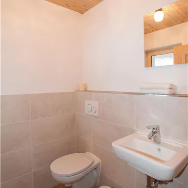 Ein modernes Badezimmer mit einer weißen Toilette und einem kleinen Waschbecken. Die Wände sind hell und die Decke hat Holzverkleidung.
