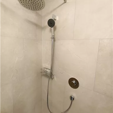 A modern shower with a large rain shower head and a handheld shower. The walls are equipped with light tiles.