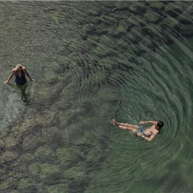 Zwei Frauen im klaren Wasser. Eine steht am Rand, während die andere entspannt auf dem Wasser treibt.
