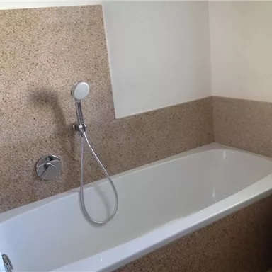Ein Badezimmer mit einer weißen Badewanne und einer modernen Dusche. Die Wände sind mit einem schlichten, hellen Material verkleidet.