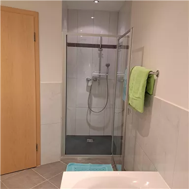 A modern bathroom with a glass shower and bright tiles. A towel in fresh green hangs next to the shower.