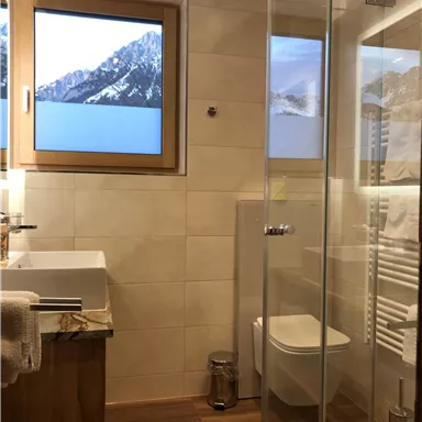 A modern bathroom with a shower and sink. A beautiful mountain landscape is visible through the window.